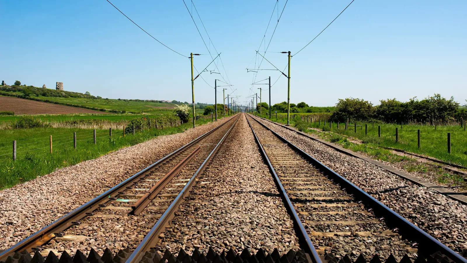 Vías de tren extendiéndose hacia el horizonte junto a un campo de hierba.