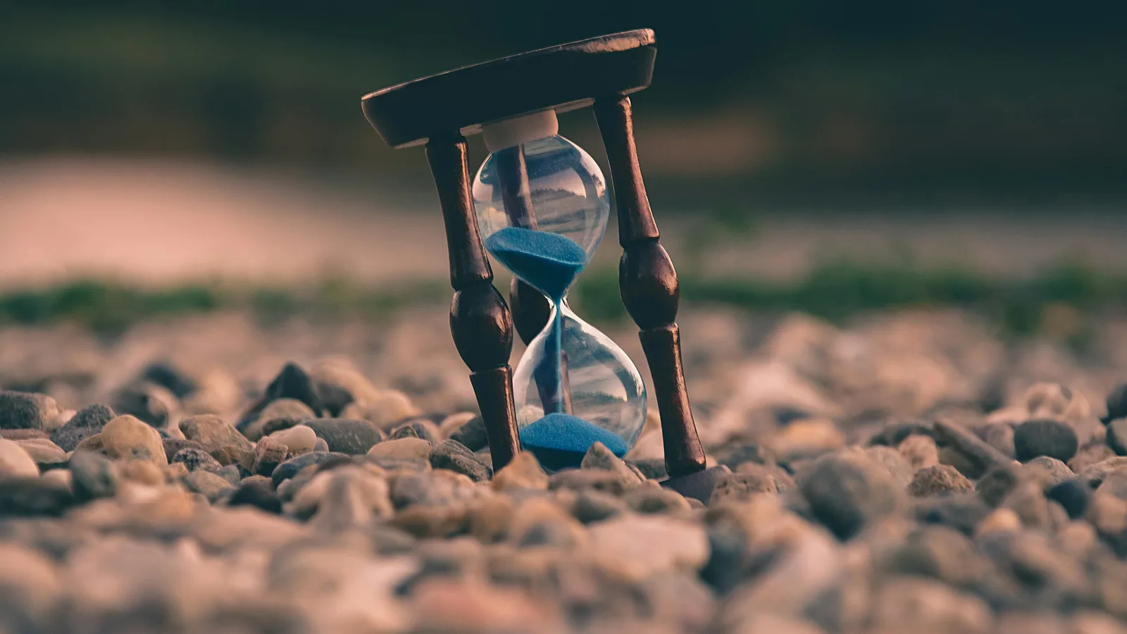 Reloj de arena sobre piedras, con la arena cayendo, en foco selectivo.