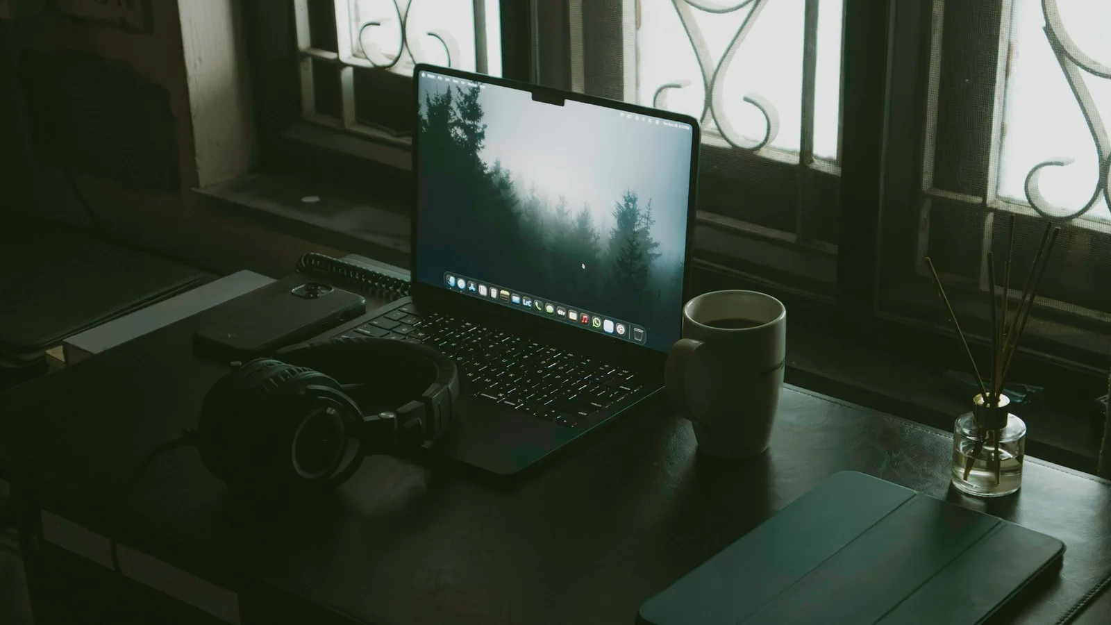 Escritorio junto a una ventana con una laptop abierta, audífonos y una taza de café.