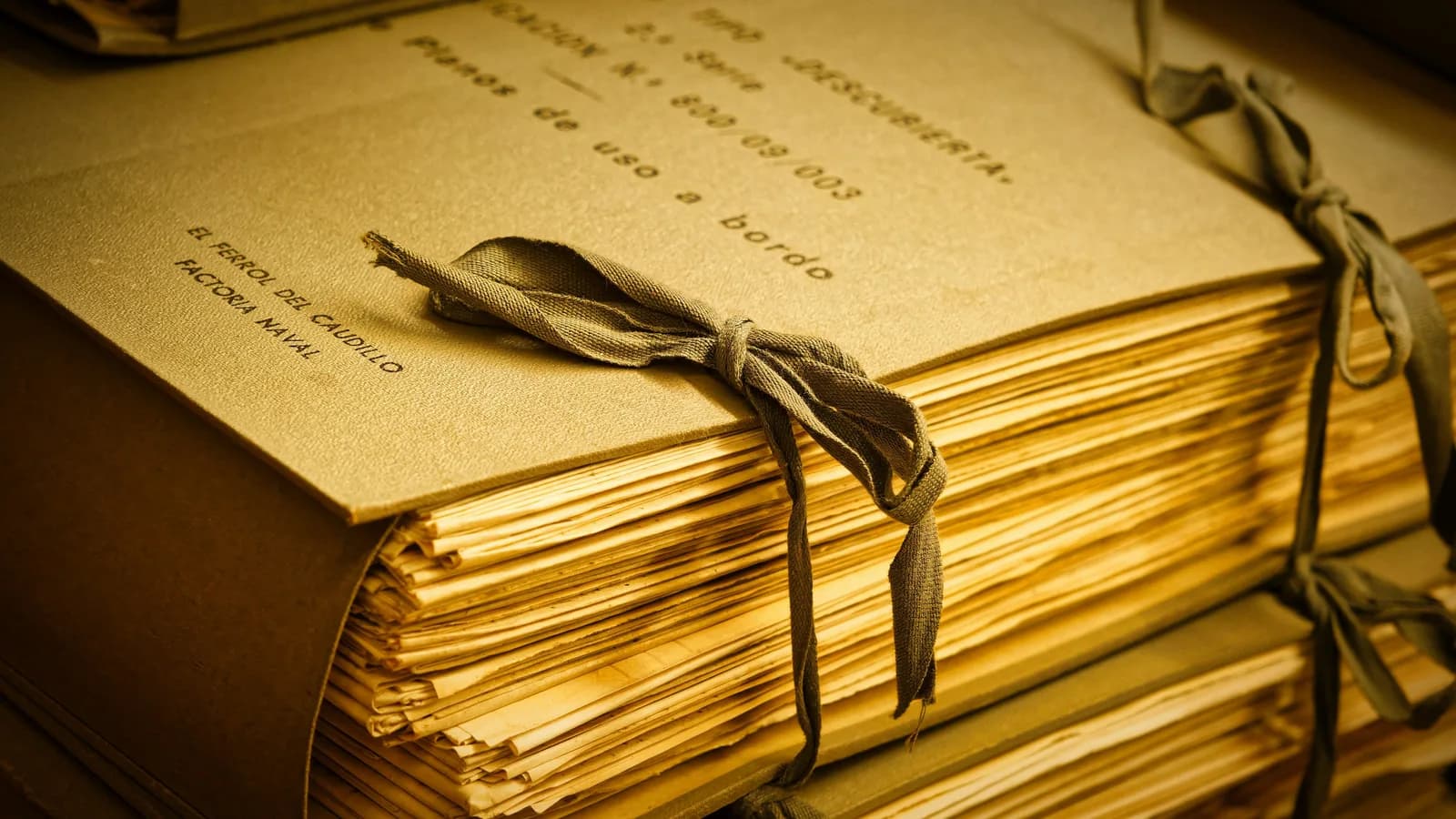 Legajo de documentos antiguos atado con cinta, apilado en la estantería de un archivo.